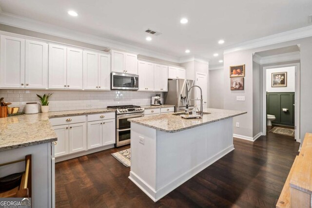 kitchen featuring sink, appliances with stainless steel finishes, white cabinetry, light stone counters, and a center island with sink