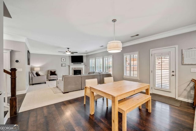 dining space with ceiling fan, ornamental molding, a fireplace, and wood-type flooring