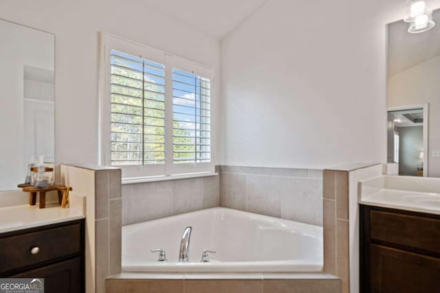 bathroom with vanity, tiled bath, and vaulted ceiling