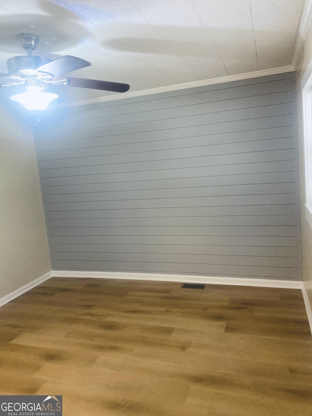 empty room featuring hardwood / wood-style flooring, ornamental molding, and wooden walls