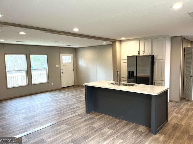 kitchen featuring sink, light hardwood / wood-style flooring, stainless steel refrigerator with ice dispenser, white cabinets, and a center island with sink