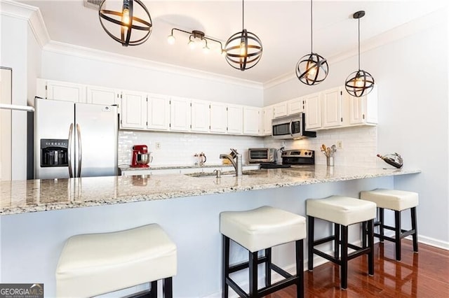 kitchen with appliances with stainless steel finishes, pendant lighting, white cabinetry, sink, and ornamental molding