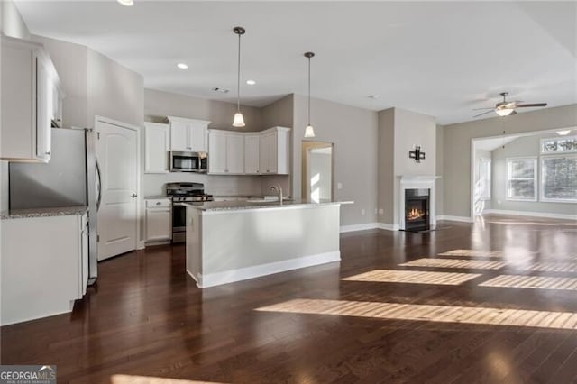 kitchen with a center island with sink, appliances with stainless steel finishes, dark hardwood / wood-style flooring, pendant lighting, and white cabinets