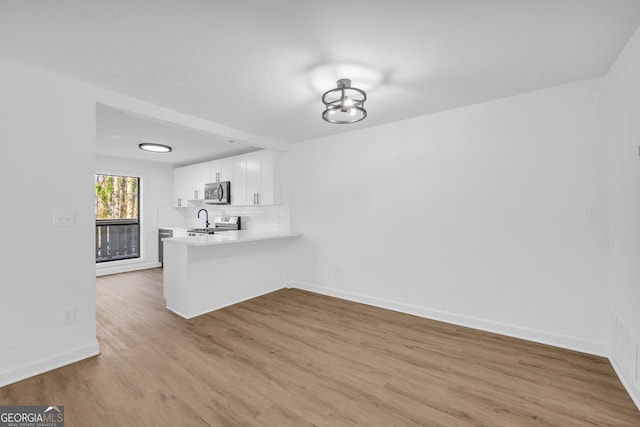 interior space featuring backsplash, appliances with stainless steel finishes, light hardwood / wood-style flooring, and white cabinets