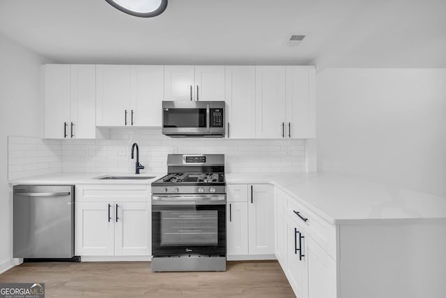 kitchen with stainless steel appliances, sink, white cabinets, and light hardwood / wood-style flooring