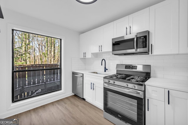 kitchen featuring sink, white cabinets, backsplash, stainless steel appliances, and light hardwood / wood-style flooring