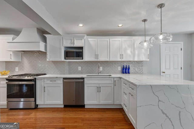 kitchen featuring sink, premium range hood, white cabinetry, stainless steel appliances, and decorative light fixtures