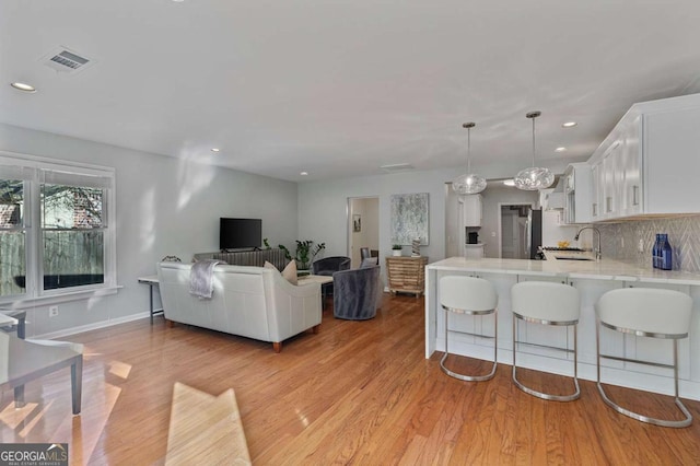 kitchen featuring white cabinetry, decorative light fixtures, kitchen peninsula, light hardwood / wood-style floors, and decorative backsplash