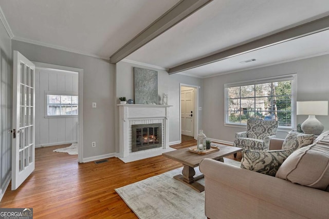 living room featuring beamed ceiling, a wealth of natural light, ornamental molding, and hardwood / wood-style floors