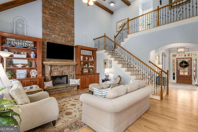 living room featuring beamed ceiling, a stone fireplace, a towering ceiling, and light hardwood / wood-style floors