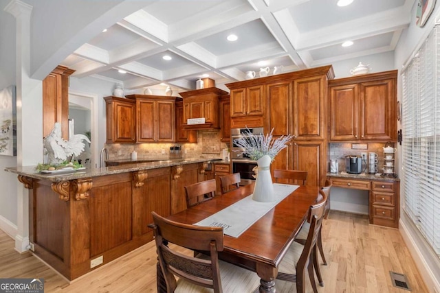 kitchen featuring coffered ceiling, light stone countertops, kitchen peninsula, and light hardwood / wood-style flooring