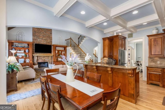 dining area featuring beamed ceiling, coffered ceiling, a fireplace, and light wood-type flooring