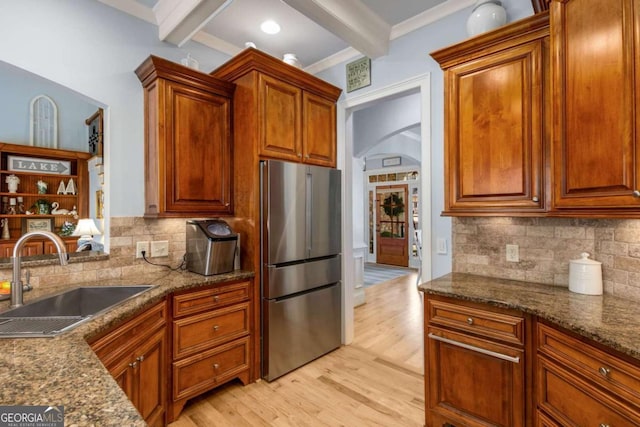 kitchen featuring sink, dark stone countertops, stainless steel fridge, beam ceiling, and light hardwood / wood-style floors