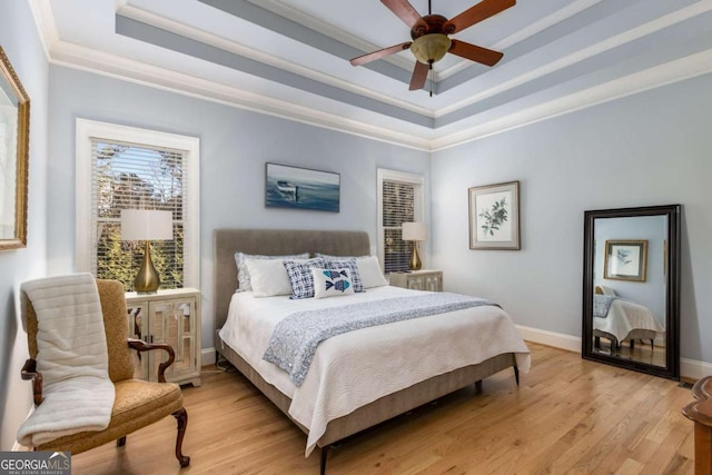 bedroom featuring ornamental molding, ceiling fan, light wood-type flooring, and a tray ceiling