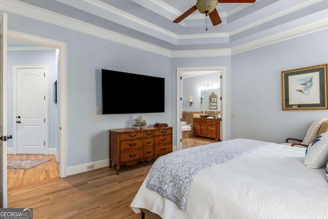 bedroom with crown molding, ensuite bath, a tray ceiling, ceiling fan, and light hardwood / wood-style floors