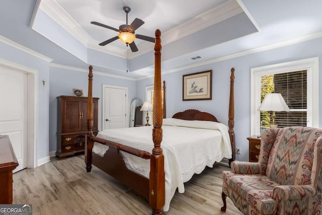 bedroom featuring crown molding, a raised ceiling, ceiling fan, and light wood-type flooring