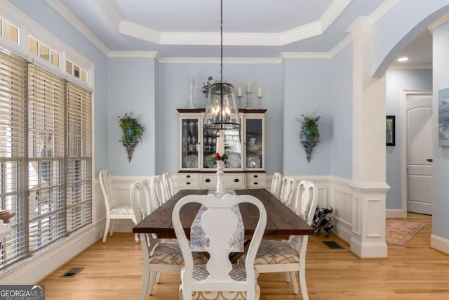 dining area featuring an inviting chandelier, ornamental molding, a raised ceiling, and light wood-type flooring