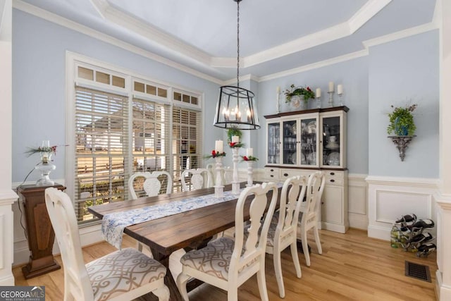 dining space featuring crown molding, a raised ceiling, and light hardwood / wood-style floors