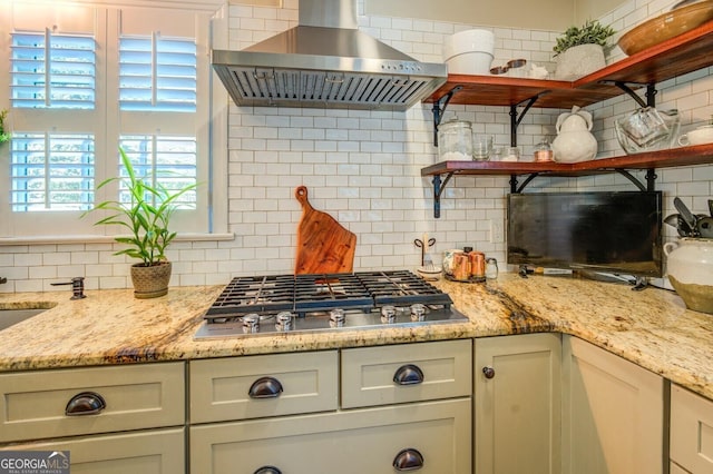 kitchen with light stone counters, stainless steel gas stovetop, backsplash, and exhaust hood