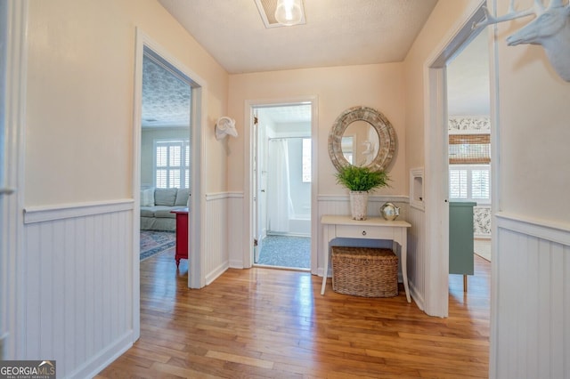 hallway with light hardwood / wood-style flooring, plenty of natural light, and a textured ceiling