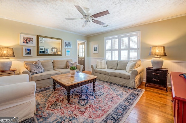 living room with hardwood / wood-style flooring, ceiling fan, crown molding, and a textured ceiling