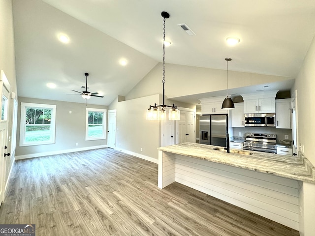 kitchen with sink, stainless steel appliances, light stone countertops, white cabinets, and decorative light fixtures