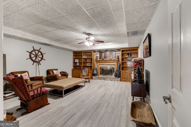 living room with built in shelves, ceiling fan, hardwood / wood-style floors, and a brick fireplace