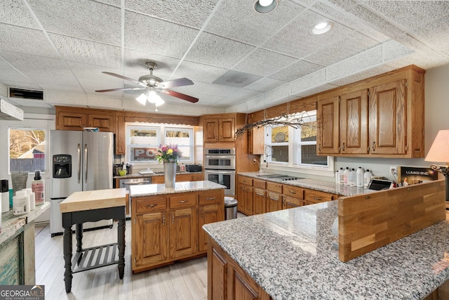 kitchen featuring light hardwood / wood-style flooring, appliances with stainless steel finishes, a kitchen island, ceiling fan, and light stone countertops