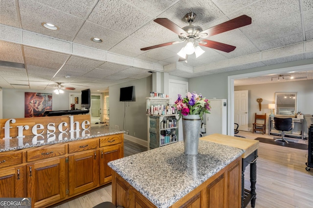 kitchen featuring light stone counters, a paneled ceiling, a kitchen island, ceiling fan, and light hardwood / wood-style floors