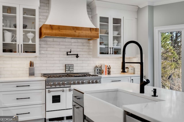 kitchen with tasteful backsplash, white cabinetry, double oven range, ornamental molding, and custom range hood