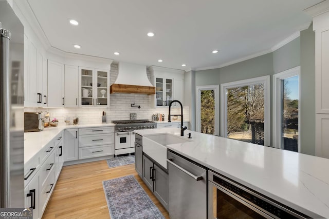 kitchen with sink, stainless steel appliances, white cabinets, and premium range hood