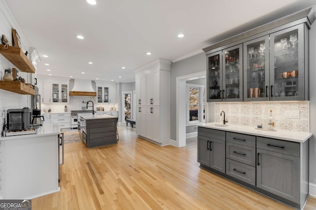 kitchen featuring high end stainless steel range, sink, gray cabinets, custom range hood, and a kitchen island with sink