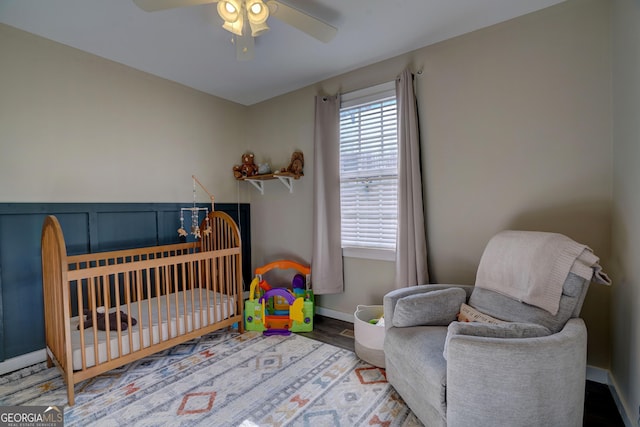 bedroom featuring a nursery area, hardwood / wood-style floors, and ceiling fan