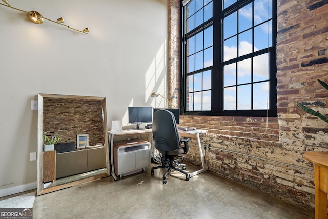 office featuring brick wall, a towering ceiling, and concrete floors