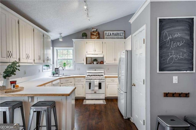 kitchen featuring vaulted ceiling, a textured ceiling, a kitchen breakfast bar, kitchen peninsula, and white appliances