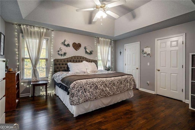 bedroom with ceiling fan, lofted ceiling, dark hardwood / wood-style floors, and a tray ceiling