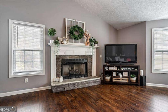 unfurnished living room featuring dark wood-type flooring, lofted ceiling, a stone fireplace, and a textured ceiling