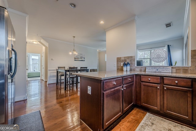 kitchen with light stone countertops, a peninsula, visible vents, stainless steel fridge with ice dispenser, and pendant lighting