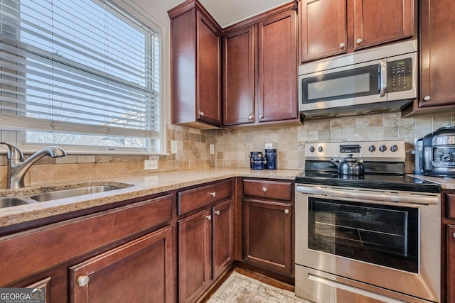 kitchen with appliances with stainless steel finishes, a sink, light stone counters, and decorative backsplash