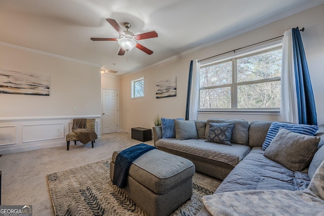 living area featuring a ceiling fan, a wainscoted wall, light carpet, and crown molding