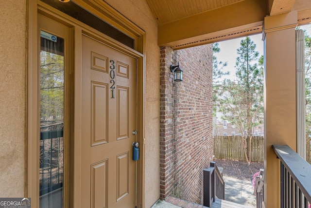 view of exterior entry with brick siding, fence, and stucco siding