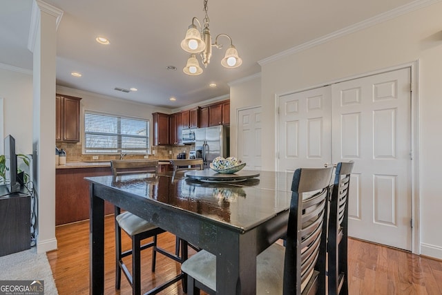 dining space with light wood finished floors, visible vents, ornamental molding, an inviting chandelier, and recessed lighting