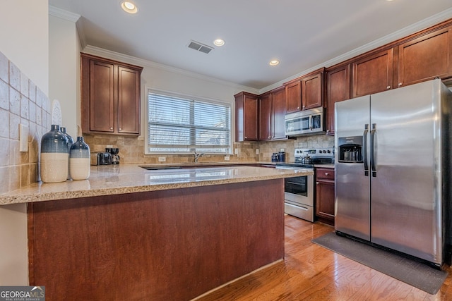 kitchen featuring light stone counters, stainless steel appliances, a peninsula, light wood-style floors, and ornamental molding