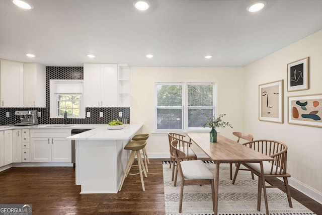 kitchen with dark wood-type flooring, a kitchen breakfast bar, kitchen peninsula, and white cabinets