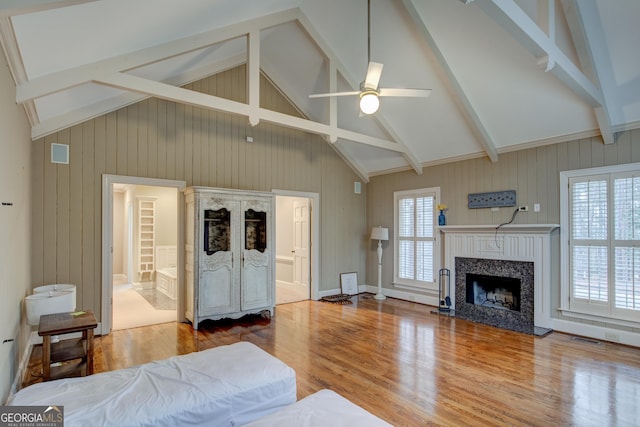 bedroom with hardwood / wood-style flooring, ensuite bath, beam ceiling, high vaulted ceiling, and a fireplace