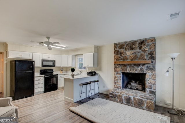 kitchen featuring a breakfast bar, white cabinetry, black appliances, kitchen peninsula, and light wood-type flooring