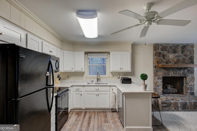 kitchen featuring sink, black appliances, light hardwood / wood-style flooring, a fireplace, and white cabinets