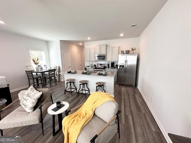 kitchen with a breakfast bar area, appliances with stainless steel finishes, dark wood-type flooring, and a center island with sink