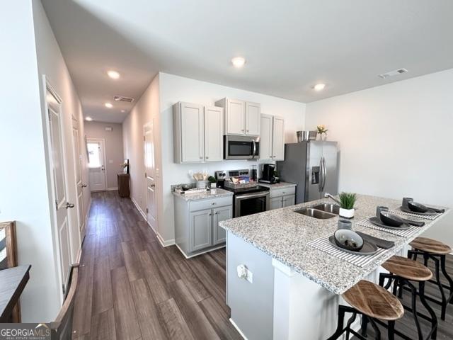 kitchen featuring sink, gray cabinets, a breakfast bar, stainless steel appliances, and light stone counters