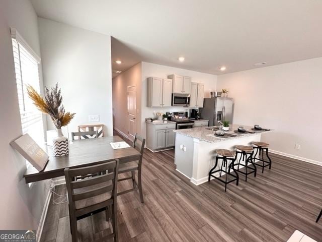 kitchen with a kitchen breakfast bar, a center island, light stone counters, stainless steel appliances, and dark wood-type flooring